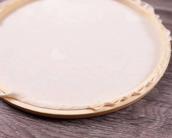 Showing the progress of gluing down the edges of the cloth in the embroidery hoop